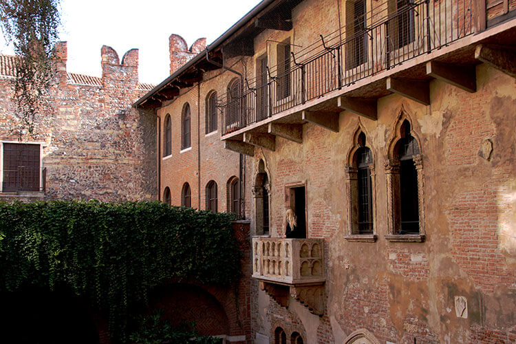 A blonde girl poses on Juliet's balcony in Verona for a photo