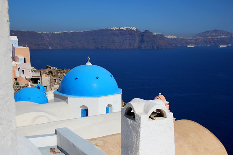 View of a blue domed church and the caldera from Oia in Santorini