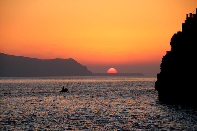 The sun blazing orange about to dip in to sea in Santorini, Greece