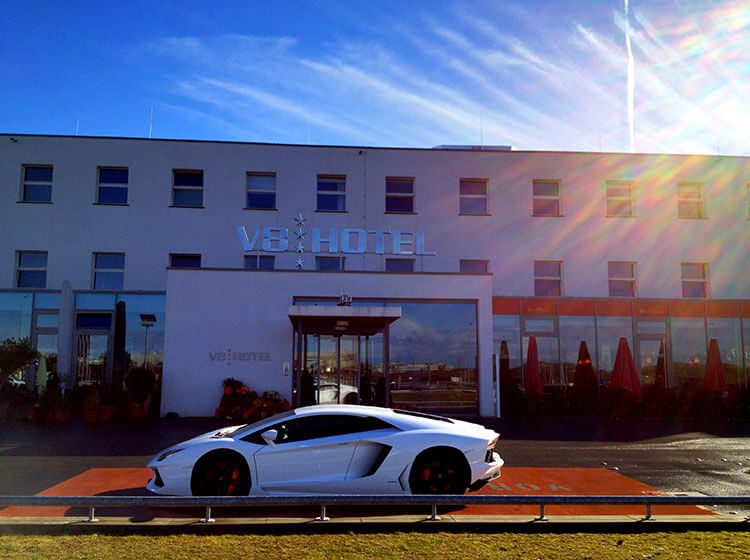 A Lamborghini is parked in front of the entrance of the V8 Hotel Motorworld Stuttgart