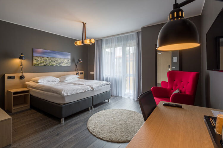 A delux room in light grays with a red armchair at Alda Hotel