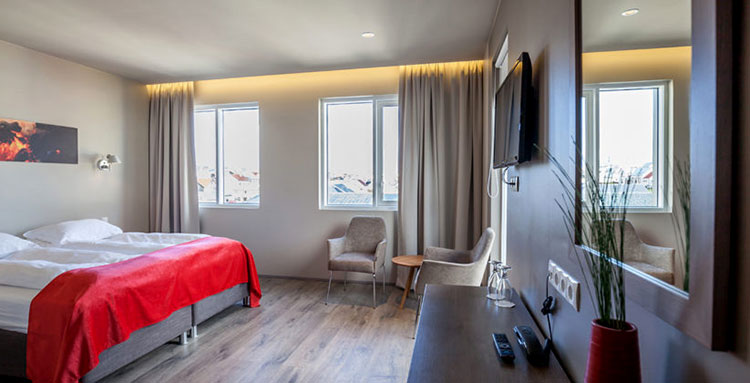 A room at Hotel Vestmannaeyjar with hard wood floors, photography of the volcano eruption and linens in gray with red accents