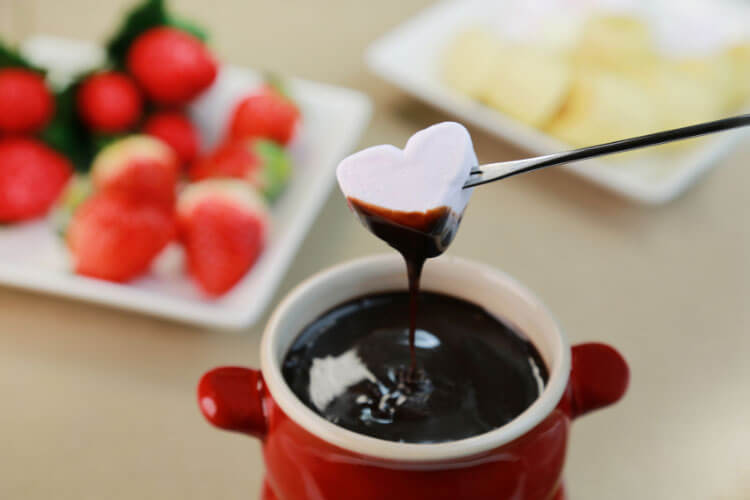 A heart-shaped marshmallow is dipped in chocolate fondue