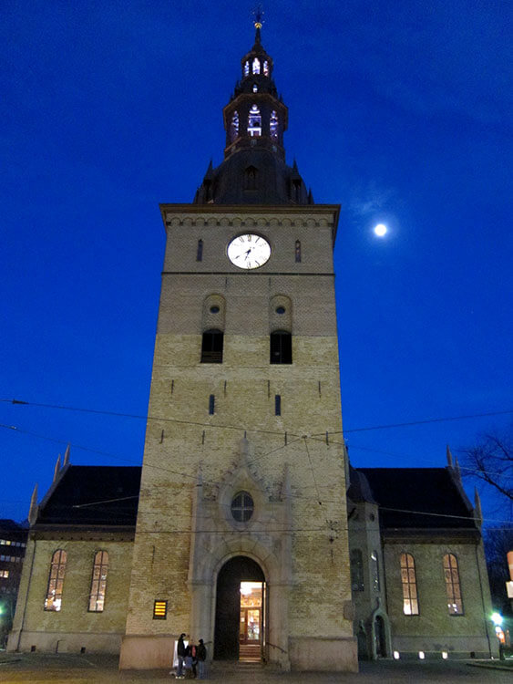 The bell tower of Oslo Domkirke with the moon rising to the right of it