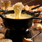 Melted cheese drips off a piece of bread on a fondue fork into a fondue pot