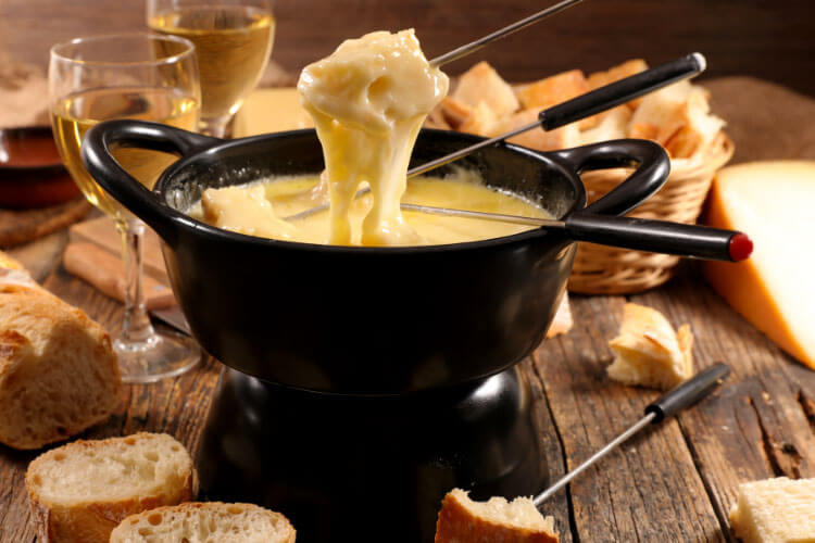 Melted cheese drips off a piece of bread on a fondue fork into a fondue pot