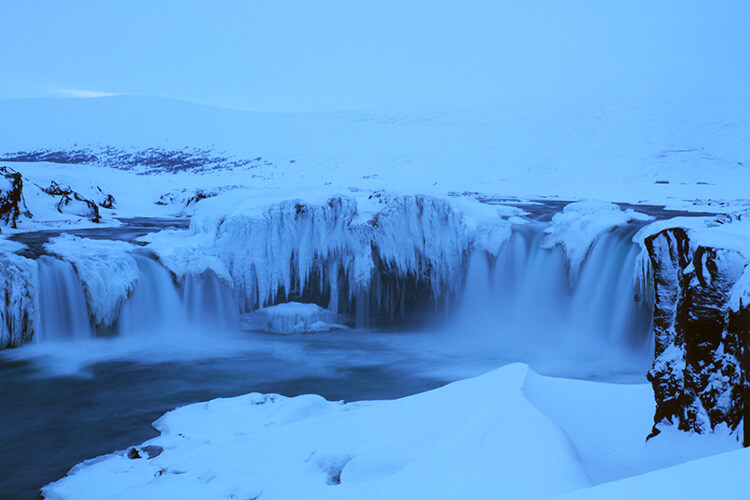 Godafoss waterfall partially frozen and snow covered in winter