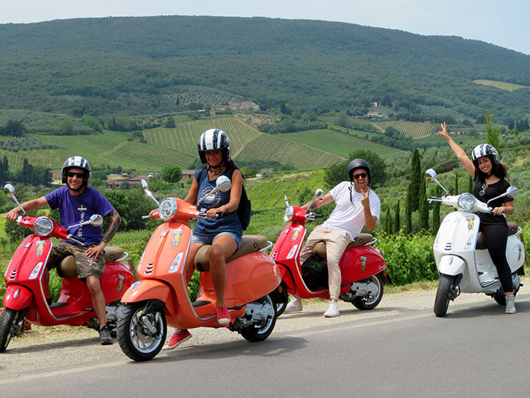 A group of four poses on their red vespas on the Vespa Tour from Florence to San Gimignano with Tuscan countryside in the background