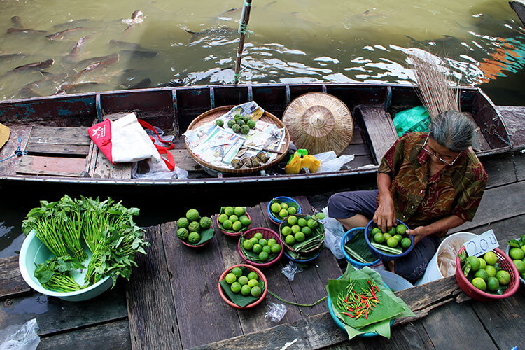 A woman sorts bowls of Thai limes in her boat at the Taling Chan Floating Market