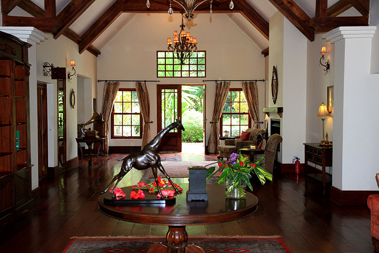 The main room in The Manor at Ngorongoro is decorated in dark woods, has a high ceiling with a chandelier and sitting areas for guests to relax