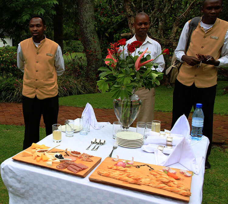 Three butlers wait with a table of snacks with cheese, bread and lemonade at The Manor at Ngorongoro 