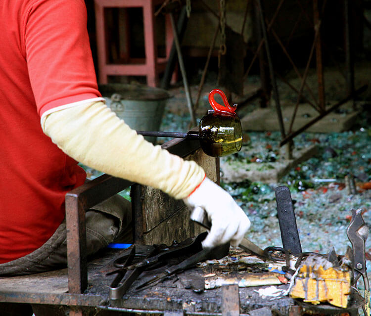 A glassblower is shaping hot glass into a coffee mug at Burka Coffee Estate