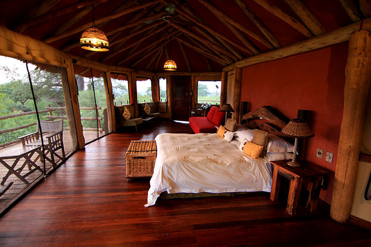 Our tree house at Tarangire Treetops with window screens surrounding it, a king size bed, and seating area