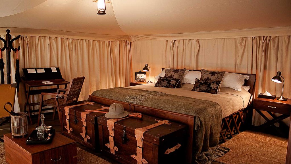 The interior of the tents at Serengeti Pioneer Camp with a 1930s style trunk, safari hat, and beige fabrics