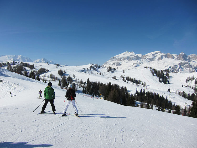 Two skiers gaze out at the Dolomites from the top of a piste at Alta Badia