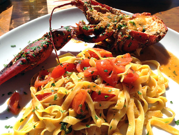 A half lobster split and placed on a plate of tagliatelle and tomatoes