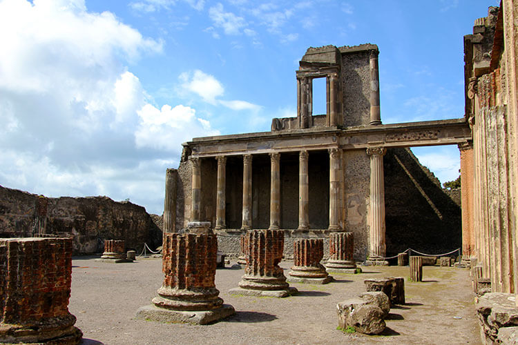 The ruins of four columns sit in front of the skeleton remains of the Basilica at Pompeii