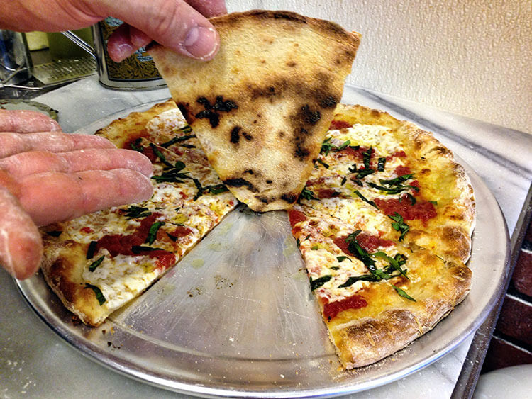 Mark holds up one slice of our margherita pizza to show a perfectly cooked pizza 