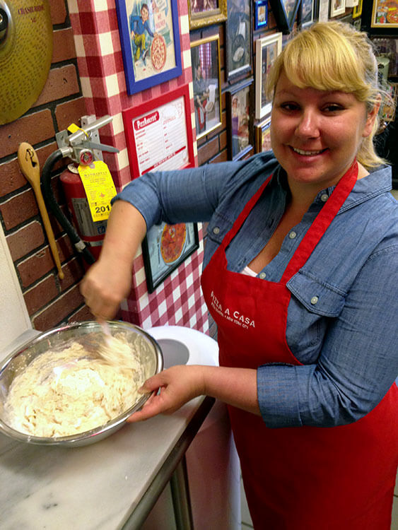 Jennifer sprinkles in some sugar to the dough mix in a mixing bowl at Pizza School NYC