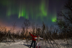 Jennifer and Tim pose under a green and purple curtain of Northern Lights in Abisko, Sweden