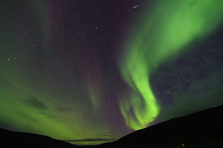 The Northern Lights appear like a candle flame shooting out of the mountain in Iceland's Westfjords