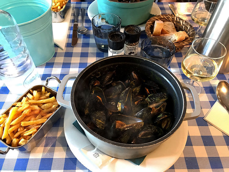 A pot of steaming mussels in curry sauce with a side of fries and wine at Les Moules du Cabanon