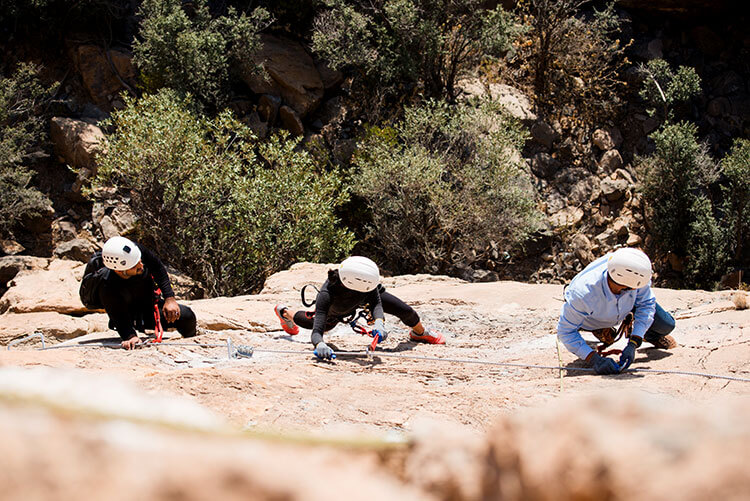 Three climbers snake along the via ferrata route along a narrow ledge on the rock face