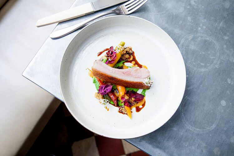 A slice of pork on a bed of colorful vegetables at Frenchie