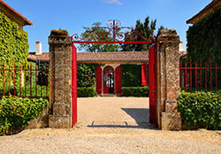 A red gate frames the single level former stone farmhouse with red doors and shutters