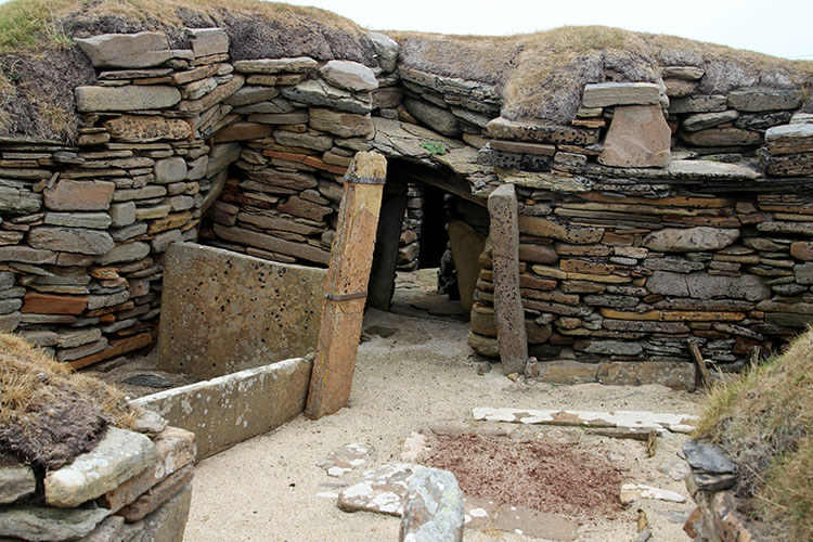 One of the stone houses at Skara Brae. Stooping down you can see multiple rooms through the door. 