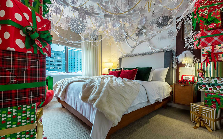 The bedroom of the Elf Suite at Club Wyndham Midtown 45 with paper snowflakes hanging from the ceiling, red and green Christmas pillows and a gift box mural wall 