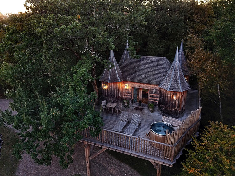 Drone view of Cabane Monbazillac tree house at dusk with lights on and the Nordic bath uncovered
