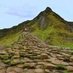 Jennifer on a raised section of Giant's Causeway with the green mountains rising up behind