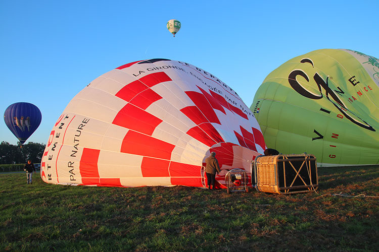 Two hot air balloons inflate while one takes off behind them in Saint-Émilion