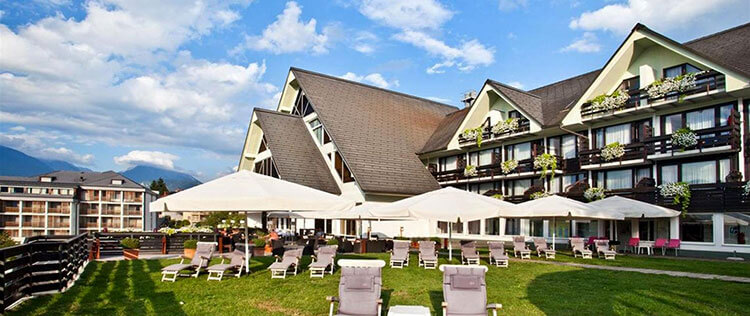 View of the exterior wooden chalet style hotel with its sun terrace overlooking Lake Bled