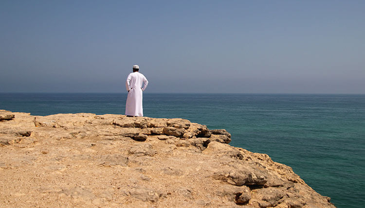 Our Anantara guide stands looking out to sea from the edge of a cliff in Salalah