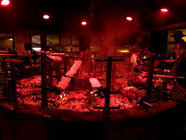 The massive barbecue pit at Carnivore with various meat and sausages cooking and smoke rising 