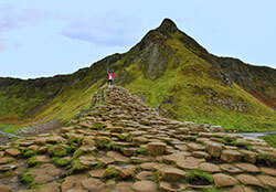 Jennifer on a raised section of Giant's Causeway with the green mountains rising up behind