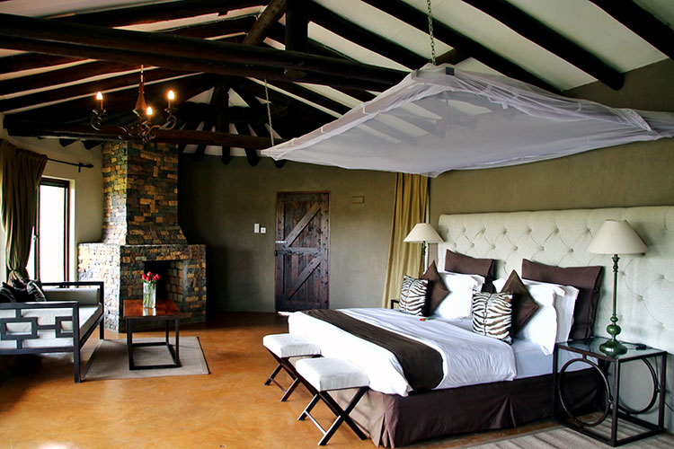 The bedroom of The Emakoko's cottage with queen size bed in brown, white and zebra print linens and a stone fireplace in the corner with a small couch for seating area in front of the fireplace