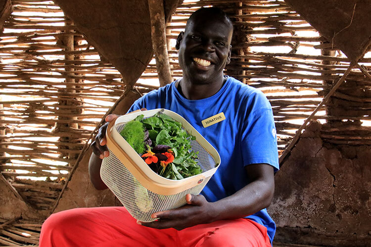 Ignatius, one of the Shamba keepers, holds the basket with the ingredients for our salad at Angama Mara