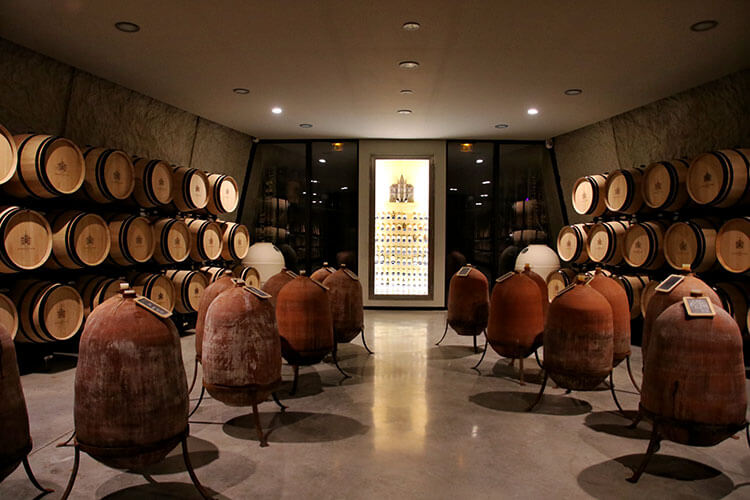 The barrel room at Château Les Carmes Haut-Brion with barrels, terracotta amphora and a small display of the owner's private collection of wine bottles