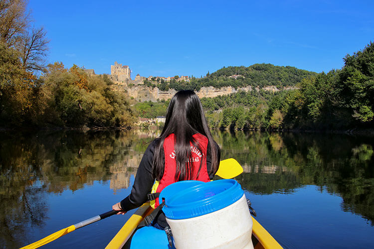Jennifer's friend AJ paddling in the front of the canoe as a castle topped village reflects on the Dordogne River