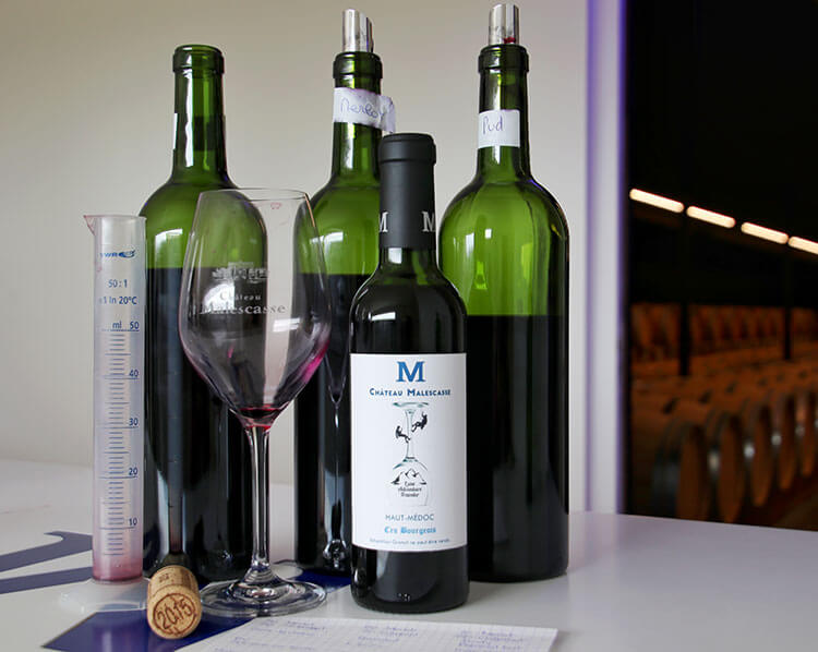 Bottles of Merlot, Cabernet Sauvignon and Petit Verdot for blending, graduated cylinder, and our finished bottle of wine at Château Malescasse