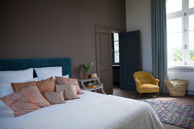 A bedroom decorated in light tones of cream with splashes of aqua looks out to the vines at Château Malescasse