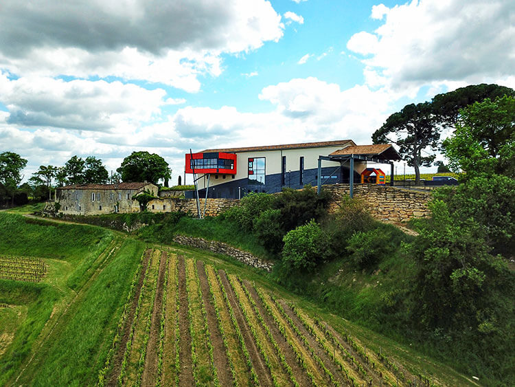 The modern winery with the orange tasting room suspended on stilts as seen from an aerial drone photo at Château La Croizille
