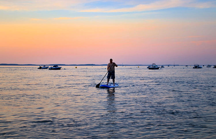 Tim paddling with boats behind him in the distance in Arcachon, France