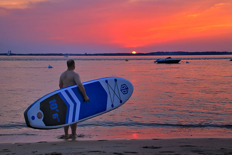 Tim carrying the SUP board while looking at the sunset at the Bassin d'Arcachon