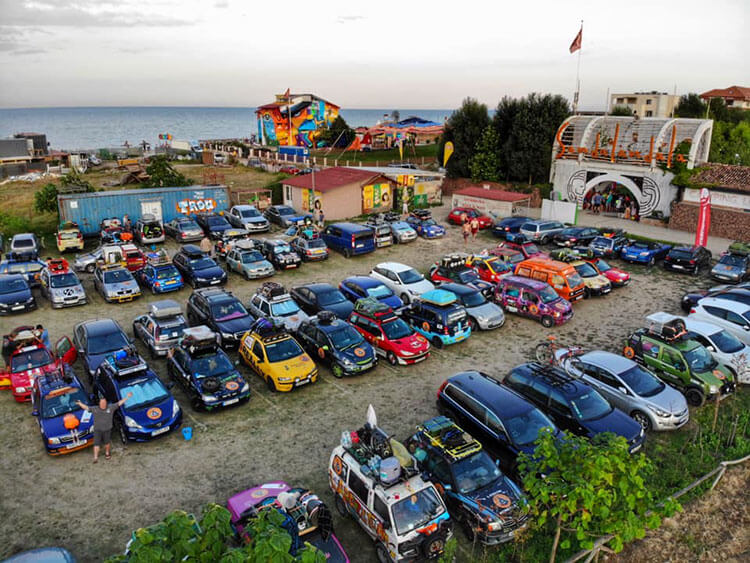 Tim poses next to his car in a dirt lot filled with Mongol Rally team cars at an official meet-up in Romania