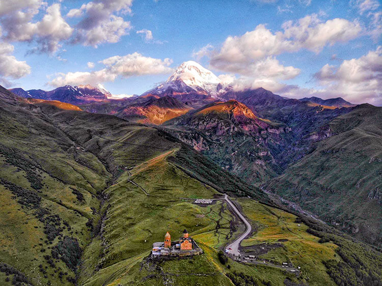 A drone aerieal of sunrise on the snow-capped Mount Kazbek with the Gergeti Church in the foreground in Georgia