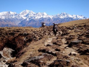 Two trekkers walk on a flat part of the trail on a clear day with the Himalayas visible behind them